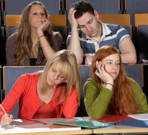  quatro alunos em um ambiente de sala de aula, três mulheres, um homem. O macho e uma fêmea parecem entediados e desatentos.