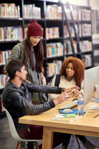 Three university students having a discussion in front of a computer monitor.